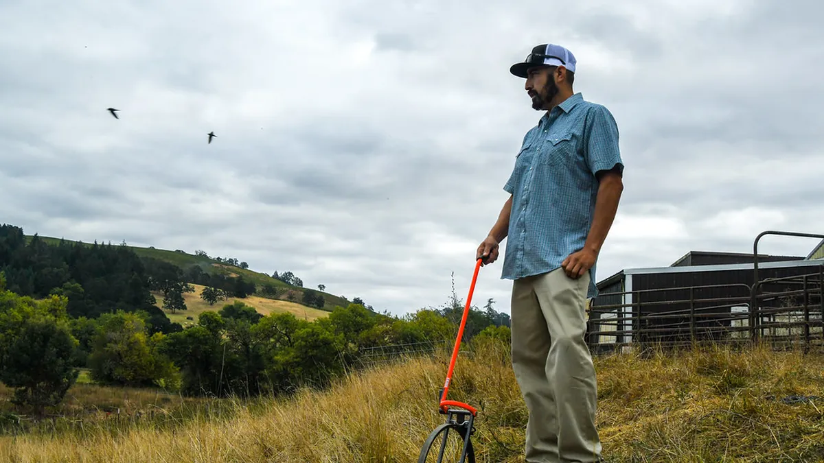 Field technician surveying a pasture layout with a measuring wheel